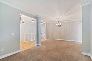 Spare room featuring a chandelier, carpet flooring, and crown molding