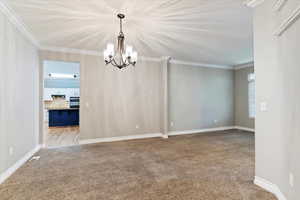 Empty room with a chandelier, light colored carpet, and crown molding