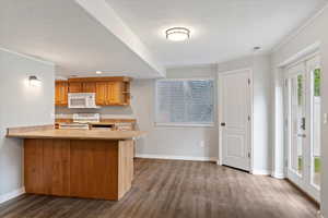 Kitchen with white appliances, dark wood-style floors, light countertops, a textured ceiling, and a peninsula
