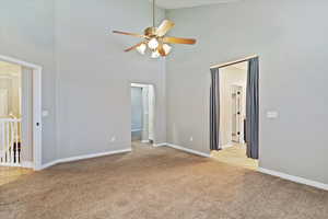 Spare room featuring a towering ceiling, light carpet, and ceiling fan
