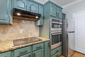 Kitchen with appliances with stainless steel finishes, decorative backsplash, under cabinet range hood, light wood finished floors, and green cabinets
