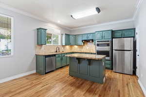 Kitchen featuring light stone counters, appliances with stainless steel finishes, crown molding, decorative backsplash, and light wood finished floors