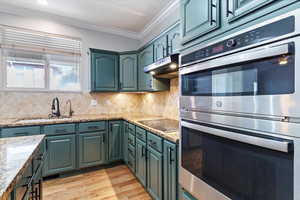 Kitchen featuring stainless steel double oven, decorative backsplash, light wood finished floors, crown molding, and light stone counters