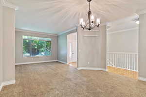 Carpeted empty room featuring crown molding and a chandelier