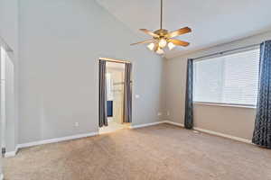Empty room with light colored carpet, ceiling fan, and high vaulted ceiling