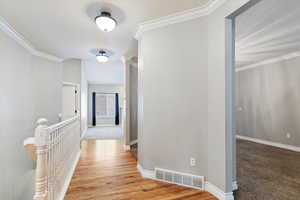 Corridor featuring an upstairs landing, crown molding, and light colored carpet