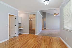 Unfurnished room featuring light wood-style floors, a chandelier, ornamental molding, ceiling fan, and healthy amount of natural light