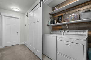 Laundry area featuring a barn door, washing machine and clothes dryer, light carpet, and a textured ceiling