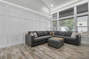 Living room with a decorative wall, plenty of natural light, light wood-style floors, high vaulted ceiling, and recessed lighting
