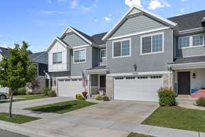 View of property with stone siding, an attached garage, stucco siding, and driveway