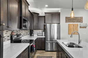 Kitchen featuring appliances with stainless steel finishes, light wood-style floors, dark brown cabinetry, decorative backsplash, and decorative light fixtures