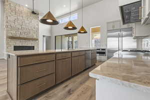 Kitchen featuring appliances with stainless steel finishes, a towering ceiling, light wood-style flooring, light stone countertops, and a fireplace