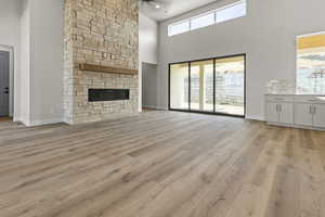 Unfurnished living room featuring a high ceiling, healthy amount of natural light, light wood finished floors, and a stone fireplace