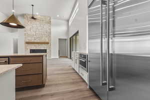 Kitchen with appliances with stainless steel finishes, a high ceiling, light wood-style floors, a stone fireplace, and decorative light fixtures