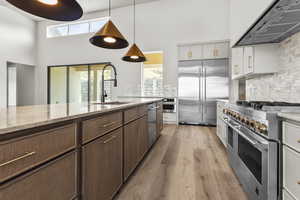 Kitchen with premium appliances, range hood, a high ceiling, light wood-style flooring, and tasteful backsplash