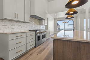 Kitchen featuring range with two ovens, custom exhaust hood, light wood finished floors, backsplash, and light stone countertops