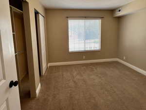 Unfurnished bedroom featuring carpet, a textured ceiling, and two closets