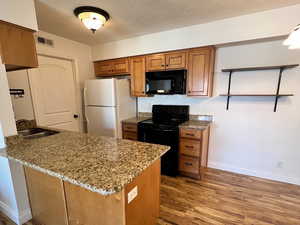 Kitchen with black appliances, brown cabinetry, dark wood finished floors, dark stone counters, and a textured ceiling