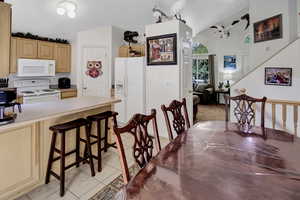 Kitchen featuring white appliances, light tile patterned floors, lofted ceiling, a kitchen breakfast bar, and light brown cabinetry