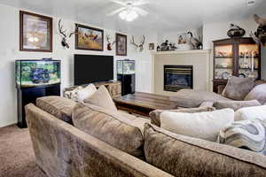 Carpeted living area with a tile fireplace, a ceiling fan, and a textured ceiling