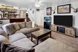 Living area with carpet floors, stairway, and a ceiling fan