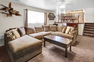 Carpeted living room with a ceiling fan and stairway