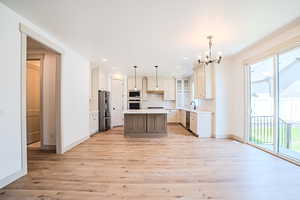 Kitchen with stainless steel appliances, a chandelier, a kitchen island, light wood-style floors, and light countertops