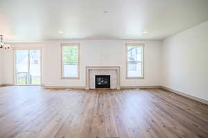 Unfurnished living room with light wood finished floors, a chandelier, and a glass covered fireplace