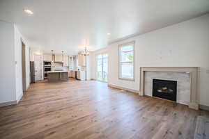 Unfurnished living room with a chandelier, light wood-style floors, a brick fireplace, and recessed lighting