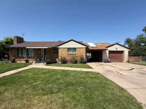 Ranch-style home with concrete driveway, a garage, a front lawn, solar panels, and a chimney