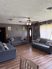 Living room with a ceiling fan, a textured ceiling, and wood finished floors
