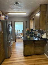 Kitchen with freestanding refrigerator, a peninsula, dark countertops, and light wood finished floors