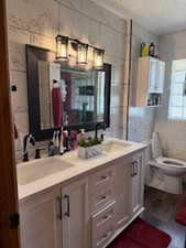 Full bathroom featuring tile walls, a textured ceiling, double vanity, and wood finished floors