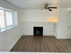 Unfurnished living room with wood finished floors, a textured ceiling, a fireplace with flush hearth, and ceiling fan