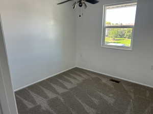 Spare room with dark carpet, ceiling fan, and healthy amount of natural light
