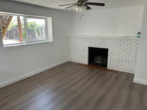 Unfurnished living room featuring dark wood-style floors, a ceiling fan, a textured ceiling, and a fireplace