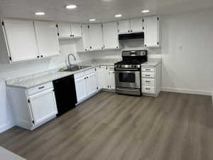 Kitchen featuring stainless steel gas range oven, black dishwasher, under cabinet range hood, white cabinetry, and recessed lighting