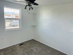 Unfurnished room featuring ceiling fan, dark colored carpet, and a textured ceiling