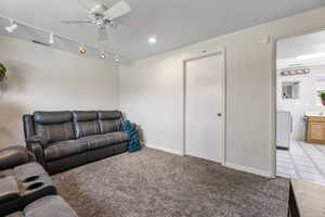 Living area with track lighting, washer / clothes dryer, ceiling fan, light carpet, and a textured ceiling