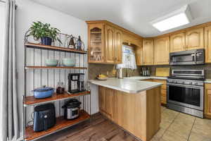 Kitchen with stainless steel appliances, decorative backsplash, light countertops, a peninsula, and open shelves