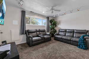 Carpeted living room with rail lighting, a ceiling fan, and a textured ceiling