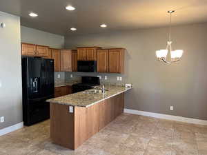 Kitchen featuring black appliances, a peninsula, brown cabinetry, a chandelier, and light stone counters