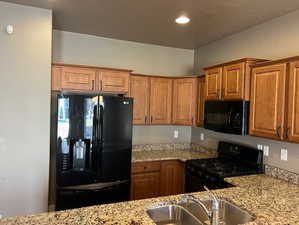 Kitchen featuring black appliances, light stone countertops, brown cabinetry, and recessed lighting