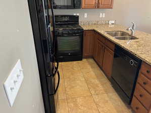 Kitchen featuring black appliances, brown cabinetry, light stone counters, and light tile patterned floors