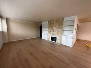 Unfurnished living room with light wood-type flooring, a stone fireplace, built in features, and crown molding