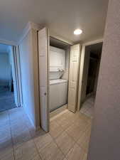Laundry area with stacked washer / drying machine, light tile patterned floors, wallpapered walls, and crown molding