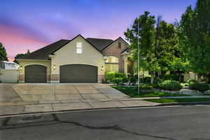 French country inspired facade featuring driveway, an attached garage, stucco siding, brick siding, and roof with shingles