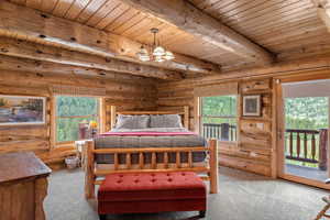 Bedroom #1 on main floor featuring a wooden ceiling with exposed beams, multiple windows, rustic walls, a chandelier, and access to outside deck