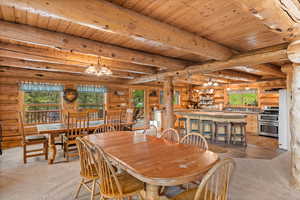 Oversized dining room featuring log walls, ceiling with exposed beams and healthy amount of natural light