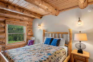 Bedroom #2 on main floor with log walls, a wood ceiling with exposed beams